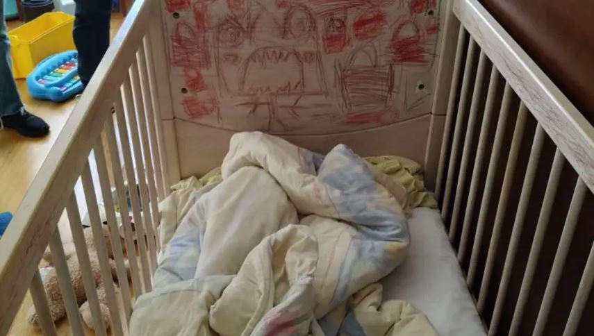 A crib with children's drawings on the headboard and bedding inside.