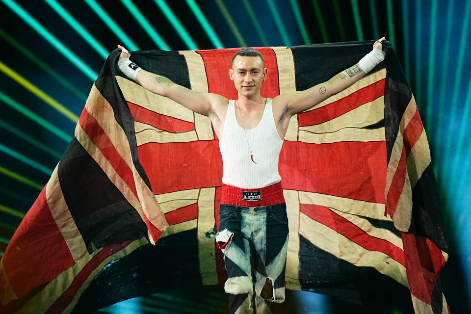 Olly Alexander holding a large UK flag on stage.