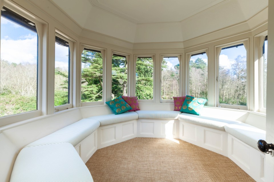Window seat with cushions overlooking a wooded area.