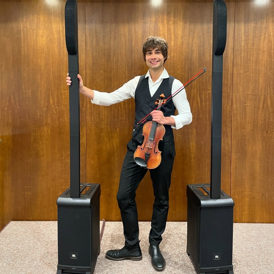 Alexander Rybak holding a violin between two speakers.