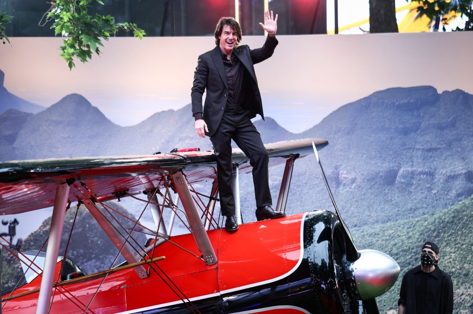 Tom Cruise waving from a red biplane at a film premiere.