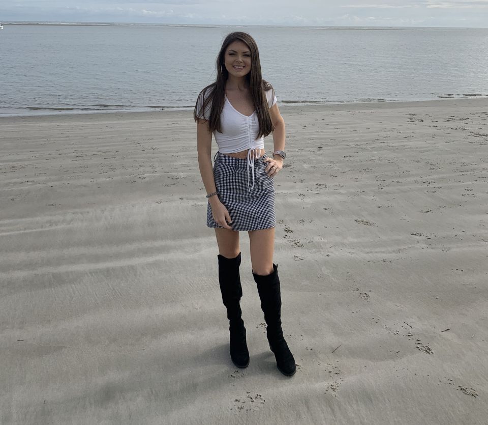 Woman in a white top and gingham skirt standing on a beach.