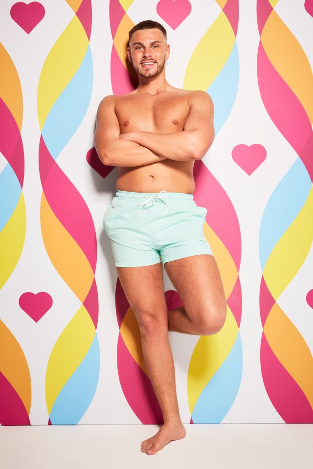 George Fensom from Love Island, standing with arms crossed.