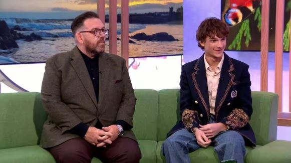 Two men sitting on a green couch during a television interview.
